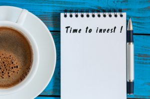 Cup of coffee, pen and notepad saying "Time to invest" on a table